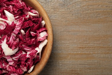 Photo of Cut radicchio in bowl on wooden table, top view. Space for text