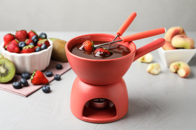 Fondue pot with chocolate and different products on grey table