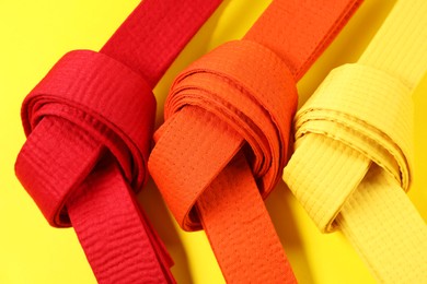 Photo of Colorful karate belts on yellow background, flat lay