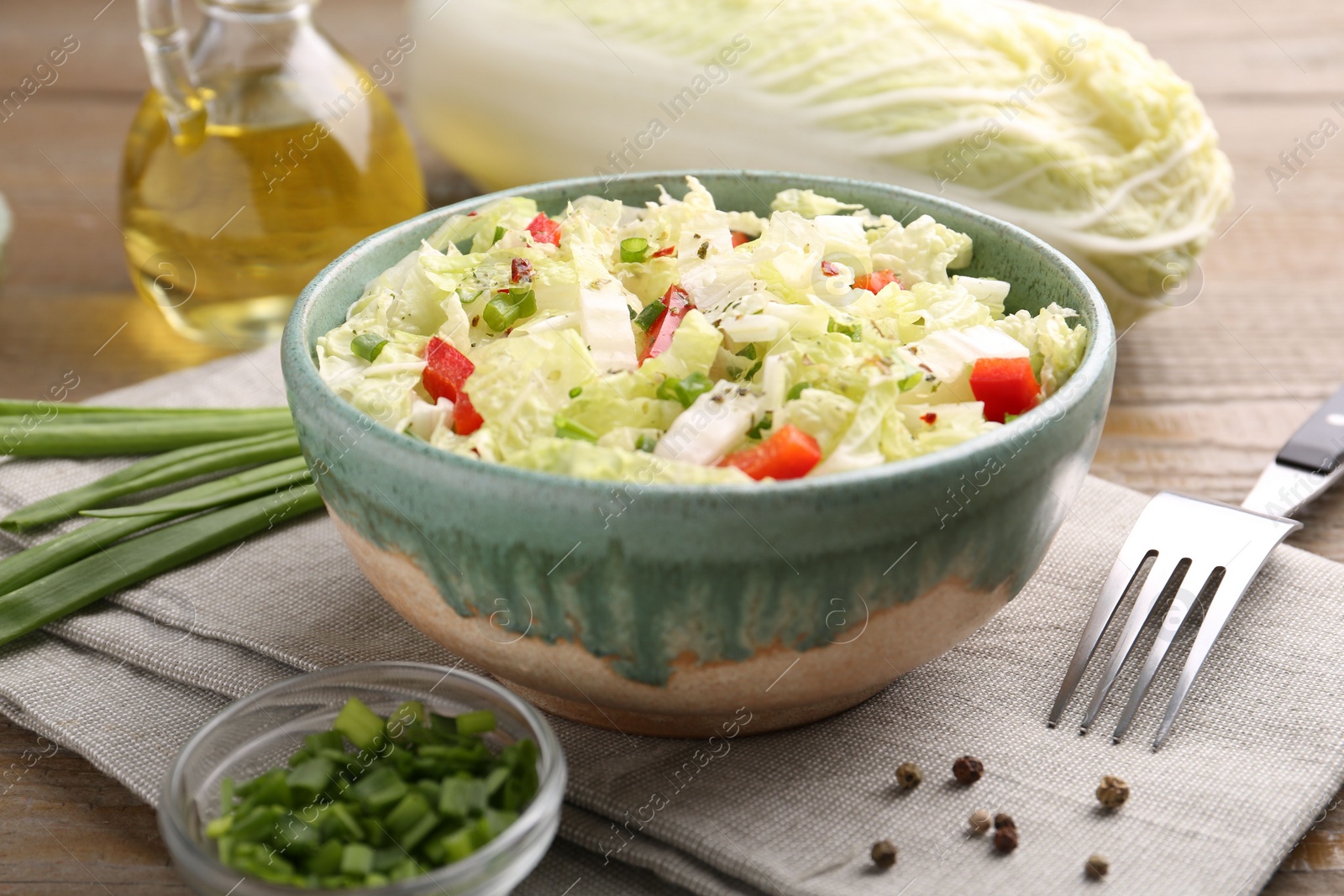 Photo of Tasty salad with Chinese cabbage in bowl, peppercorns and green onion on wooden table, closeup