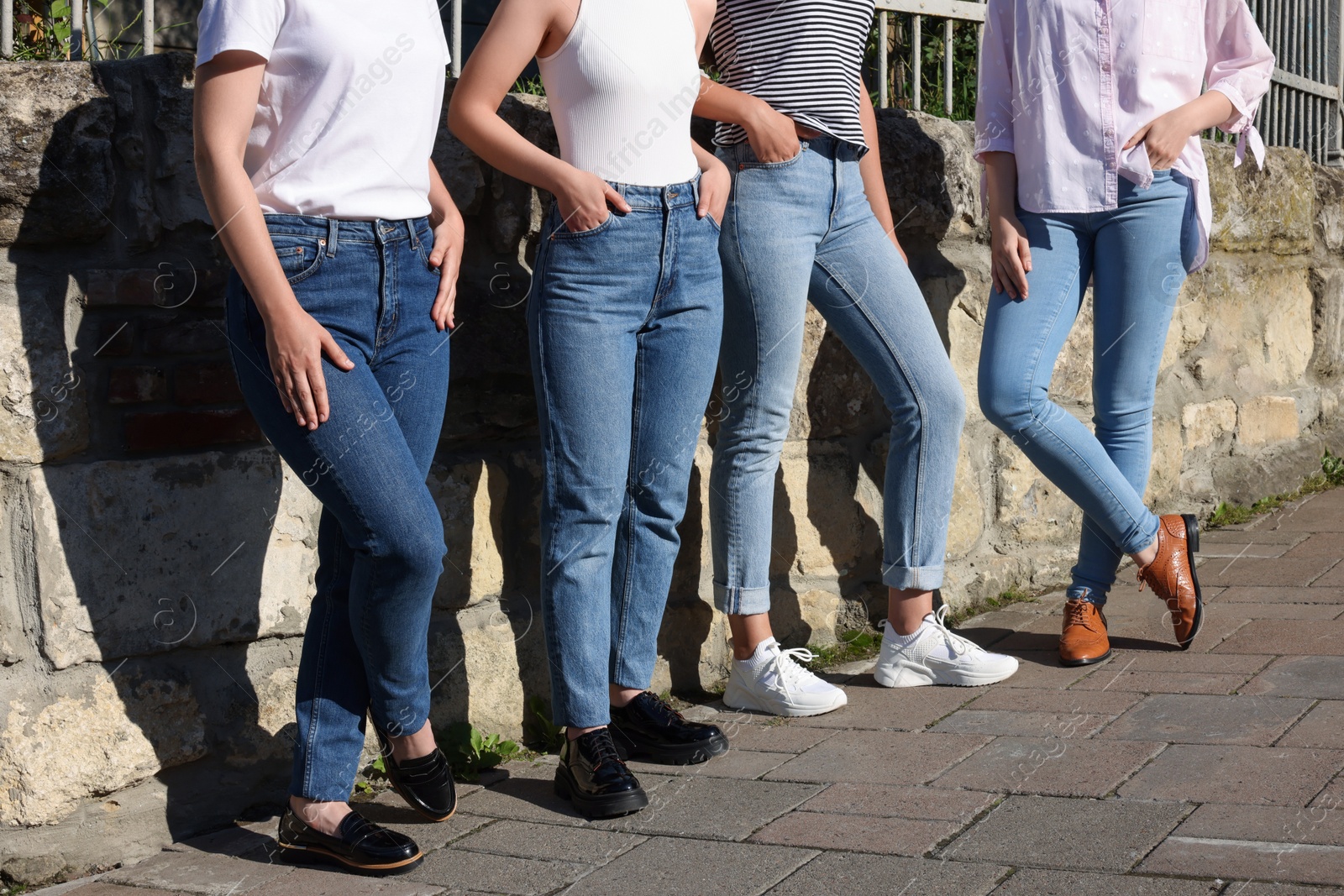 Photo of Women in stylish jeans near stone wall outdoors on sunny day, closeup