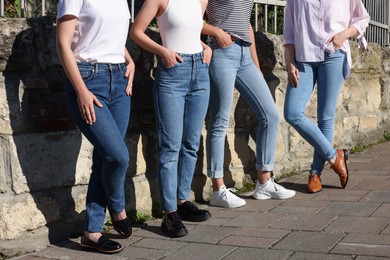 Photo of Women in stylish jeans near stone wall outdoors on sunny day, closeup