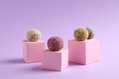 Photo of Minimalistic composition with different delicious vegan candy balls and pink cubes on violet background