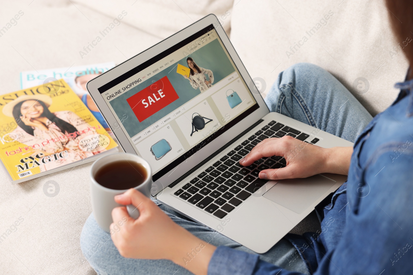 Photo of Woman with cup of tea shopping online during sale on laptop at home, closeup