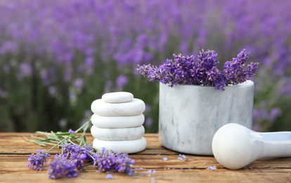 Photo of Spa stones, fresh lavender flowers and white marble mortar on wooden table outdoors, closeup