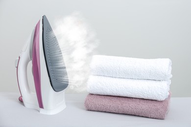 Modern iron with steam and folded towels on white table