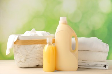 Bottles of laundry detergents and clean clothes on white wooden table