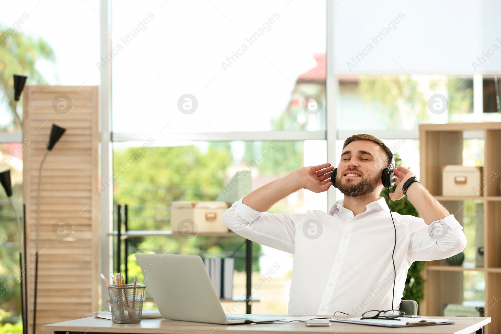 Photo of Young man listening to music while working with laptop at table in office