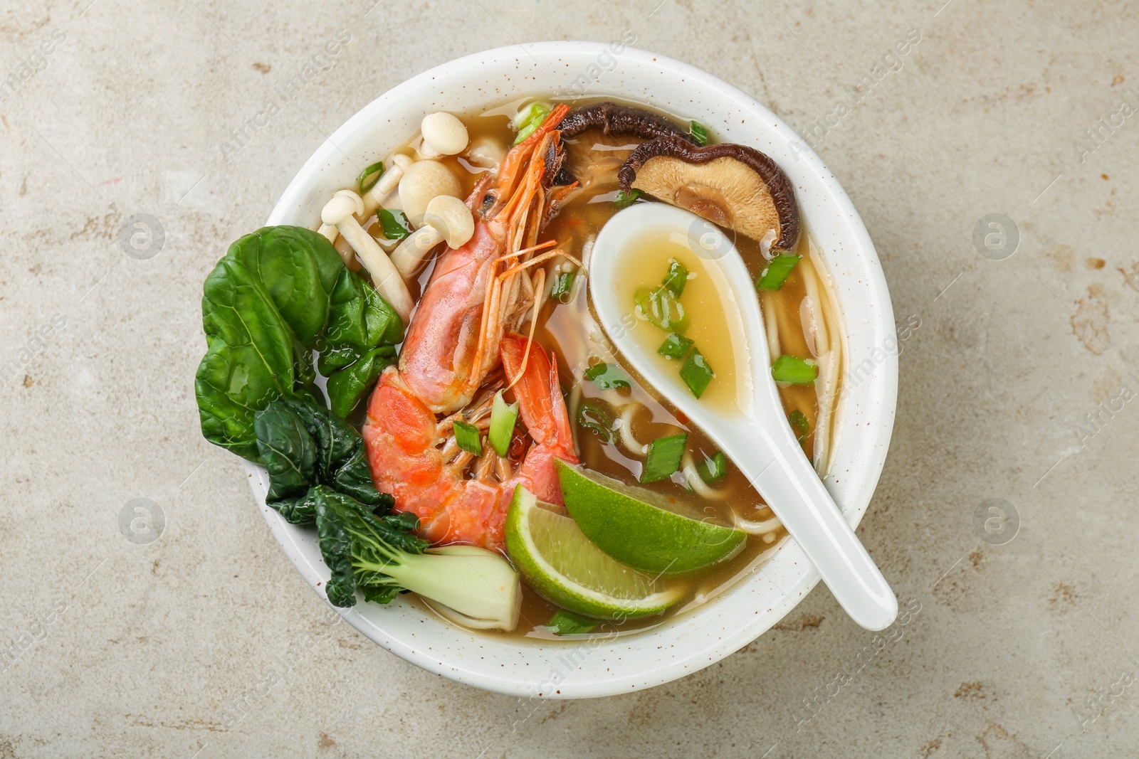 Photo of Delicious ramen with shrimps, mushrooms and spoon in bowl on light textured table, top view. Noodle soup