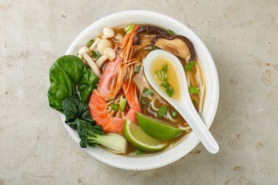 Photo of Delicious ramen with shrimps, mushrooms and spoon in bowl on light textured table, top view. Noodle soup