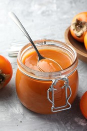 Photo of Delicious persimmon jam and fresh fruits on grey table