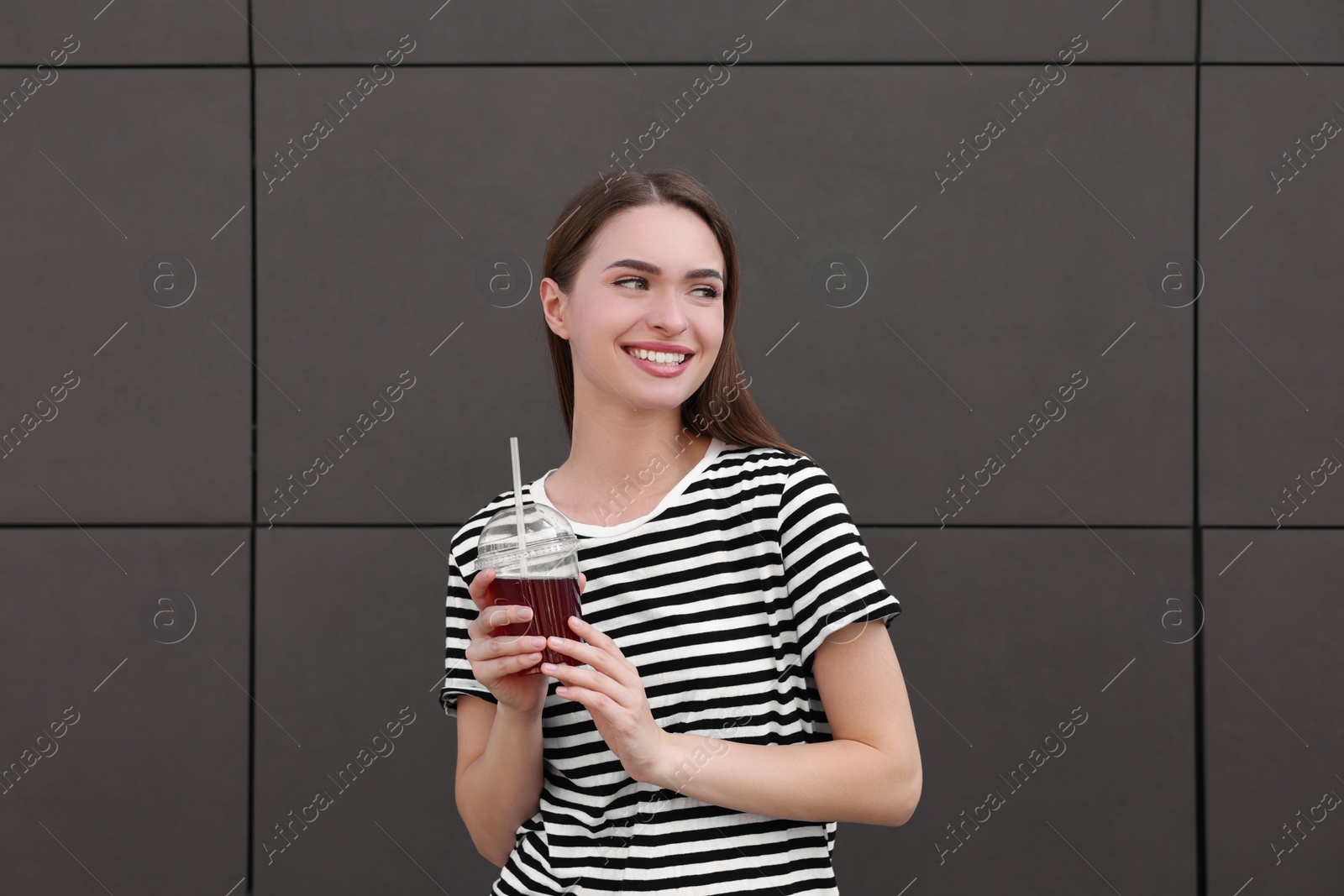 Photo of Young woman with plastic cup of fresh juice near brown wall