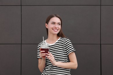 Photo of Young woman with plastic cup of fresh juice near brown wall