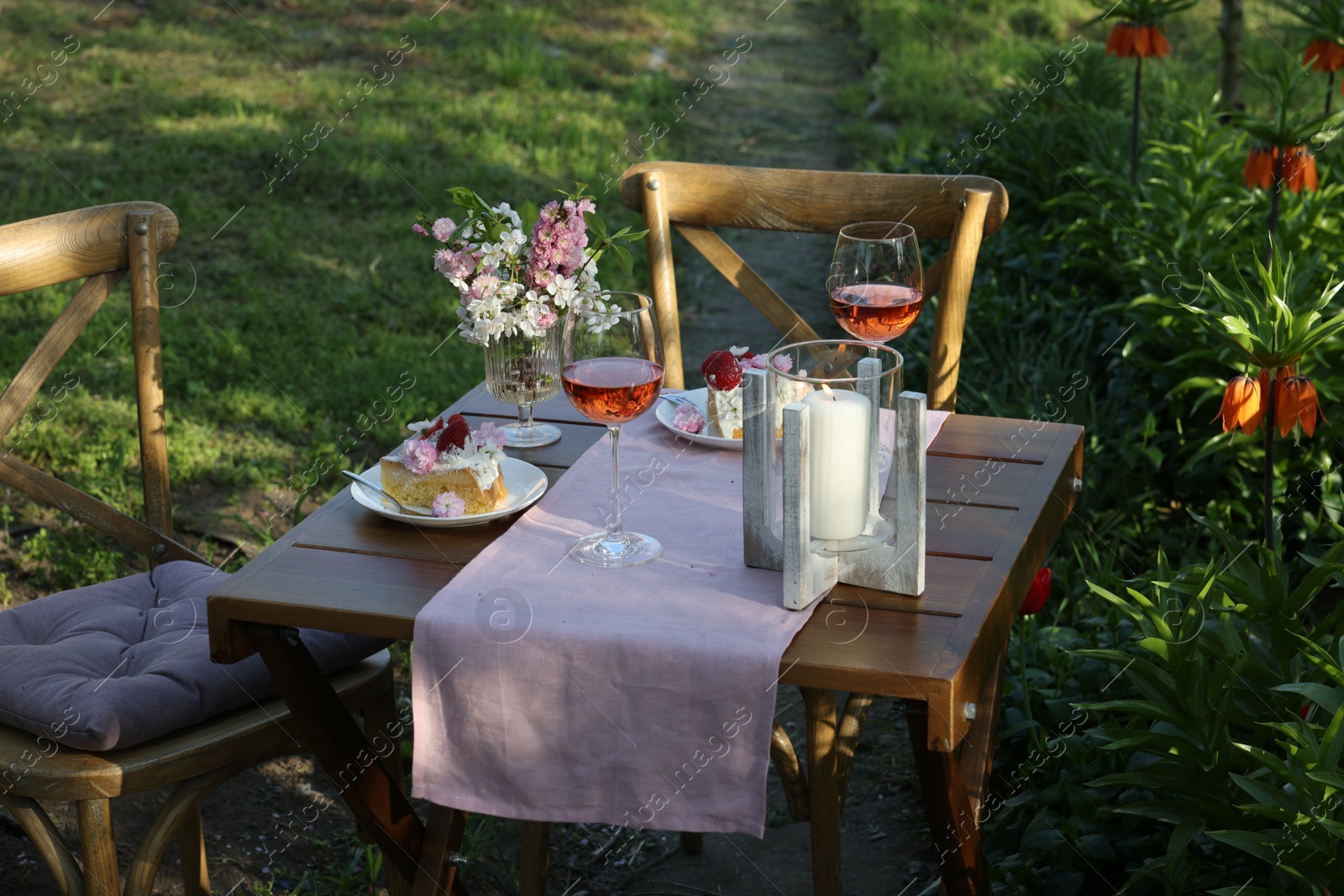 Photo of Vase with spring flowers, wine and cake on table served for romantic date in garden