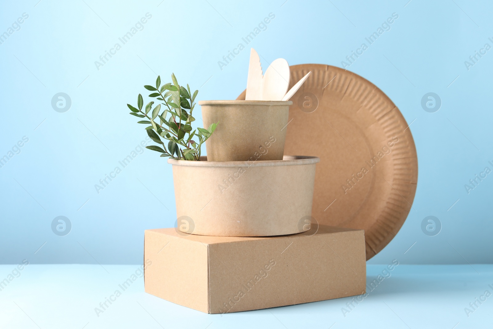 Photo of Eco friendly food packaging. Paper containers, tableware and green twig on white table against light blue background