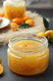 Photo of Delicious kumquat jam in glass jar on grey table