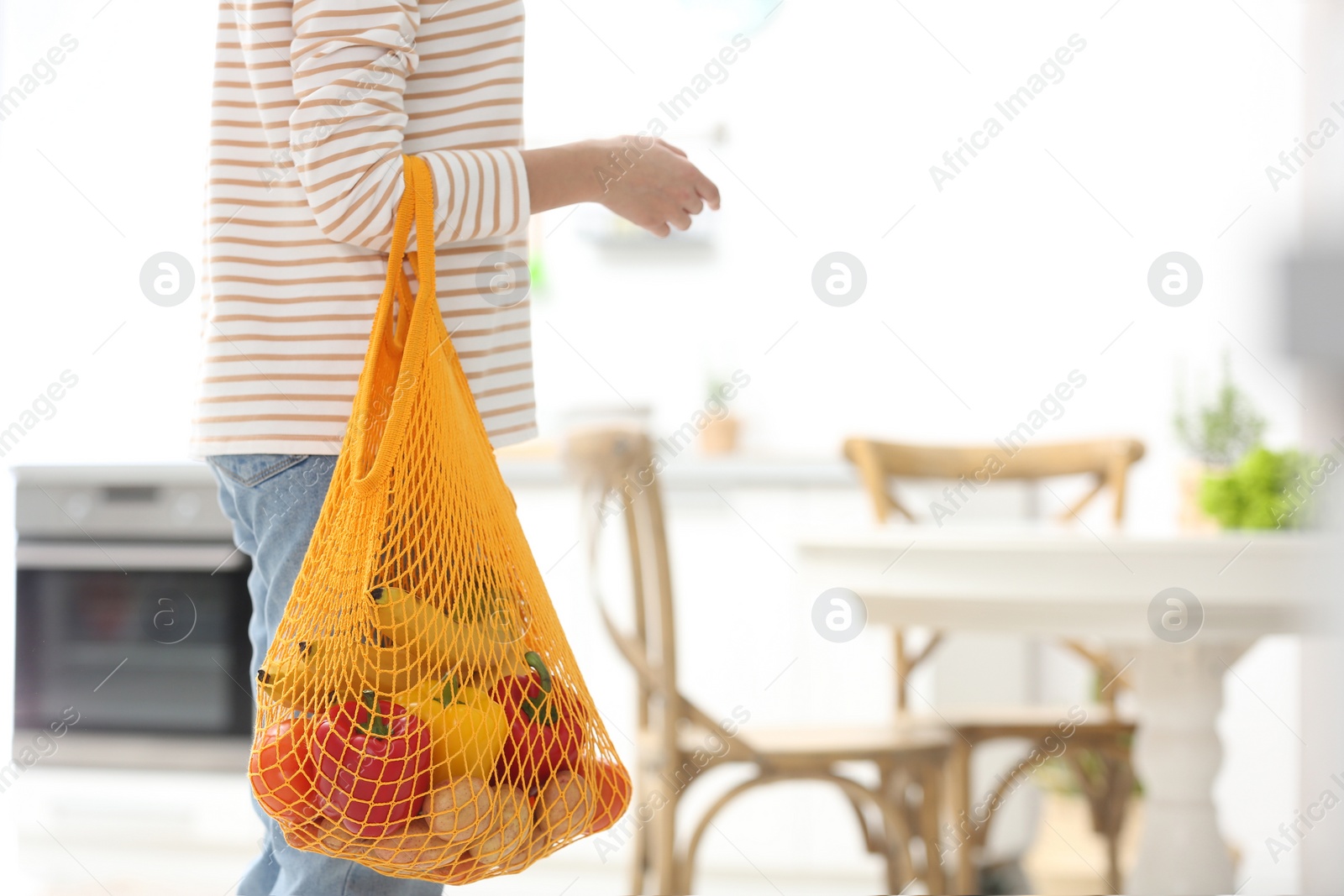 Photo of Woman with net bag full of fruits and vegetables in kitchen, closeup. Space for text