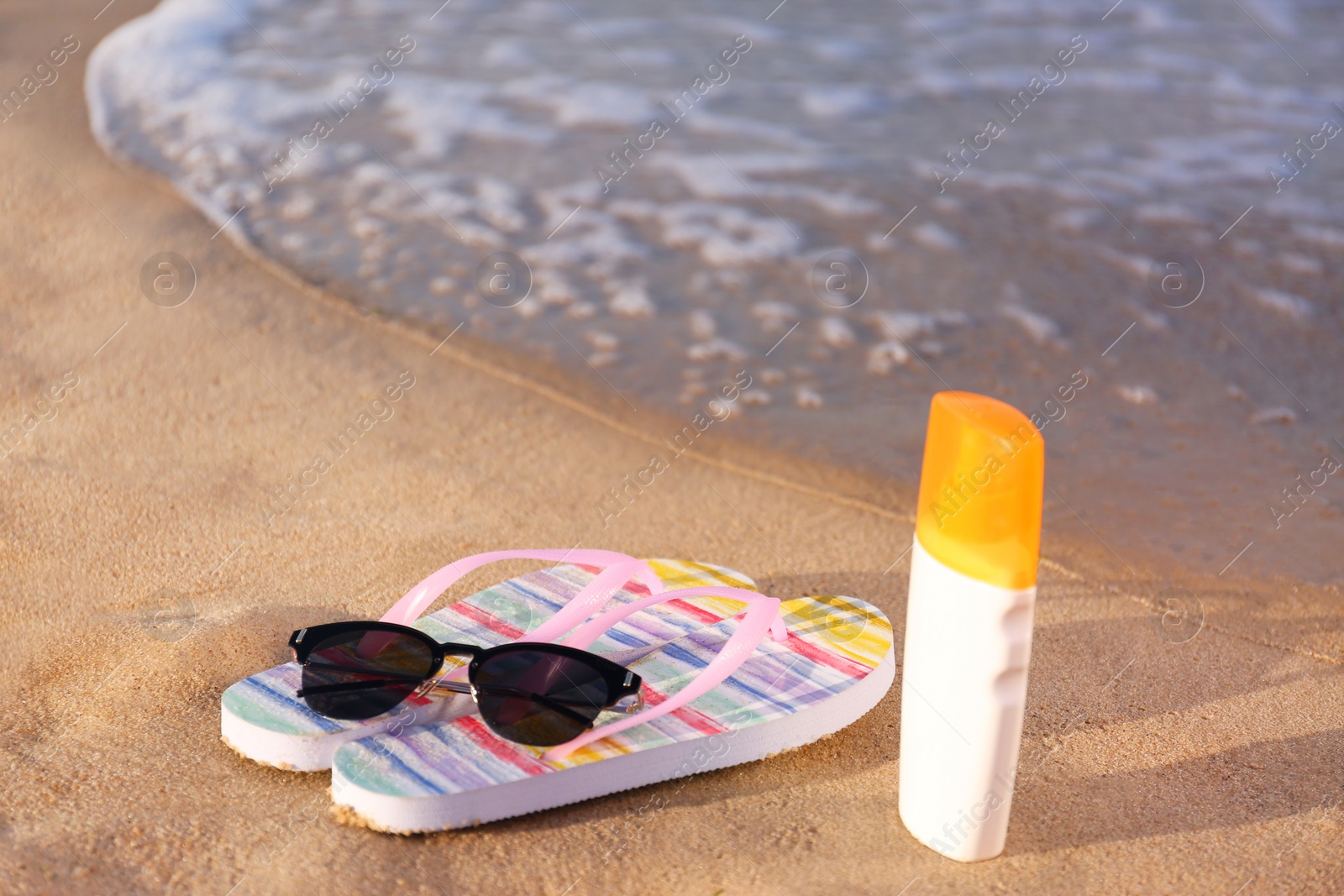 Photo of Flip flops and beach accessories on sand near sea. Space for text