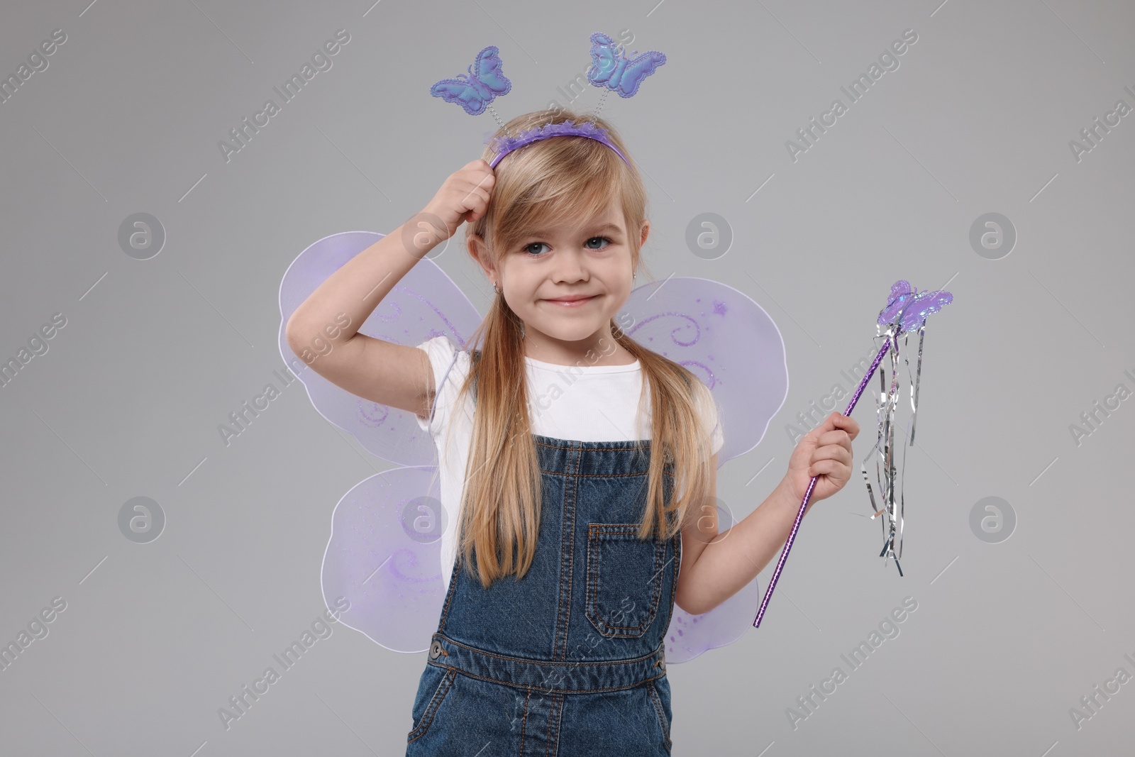 Photo of Cute little girl in fairy costume with violet wings and magic wand on light grey background