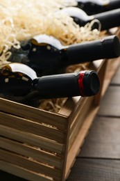 Crate with bottles of wine on wooden background, closeup