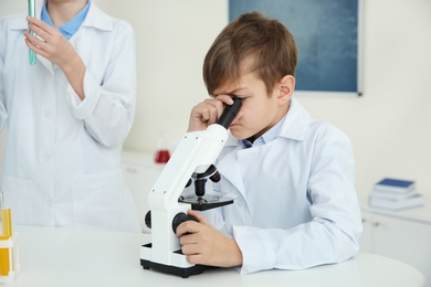 Pupil looking through microscope at table in chemistry class