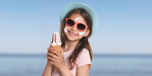 Adorable little girl with sun protection cream on face at beach, banner design 