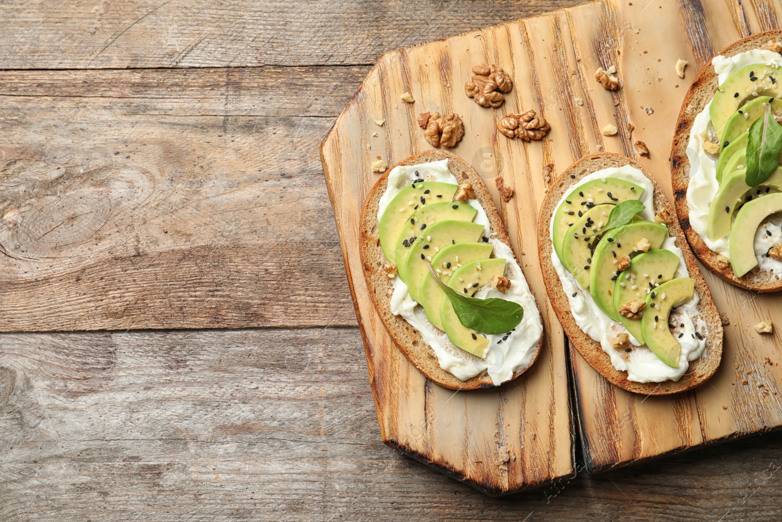 Photo of Board with avocado bruschettas on wooden table, flat lay. Space for text