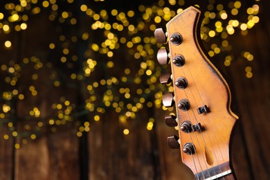 Closeup view of guitar at wooden table against blurred lights, space for text