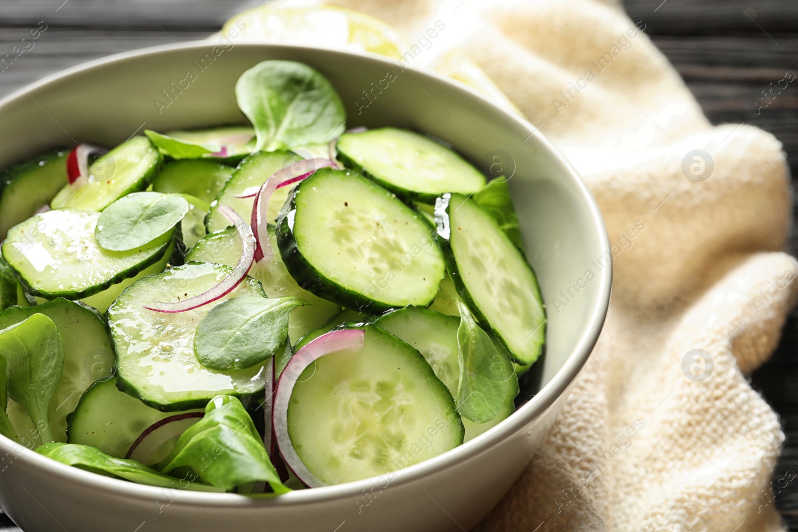 Photo of Delicious cucumber salad with onion and spinach in bowl on table, closeup