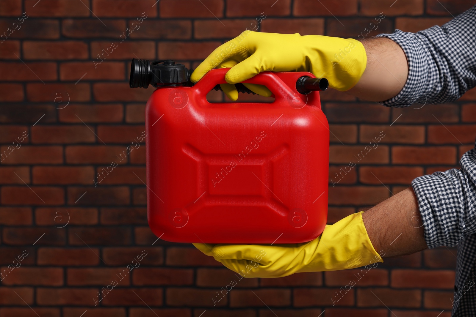 Photo of Man holding red canister against brick wall, closeup