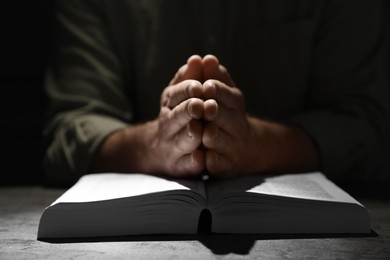 Photo of Religion. Christian man praying over Bible at table, closeup