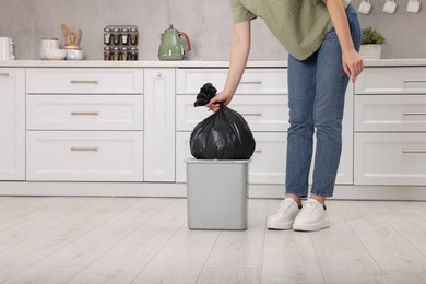 Photo of Woman taking garbage bag out of trash bin in kitchen, closeup. Space for text