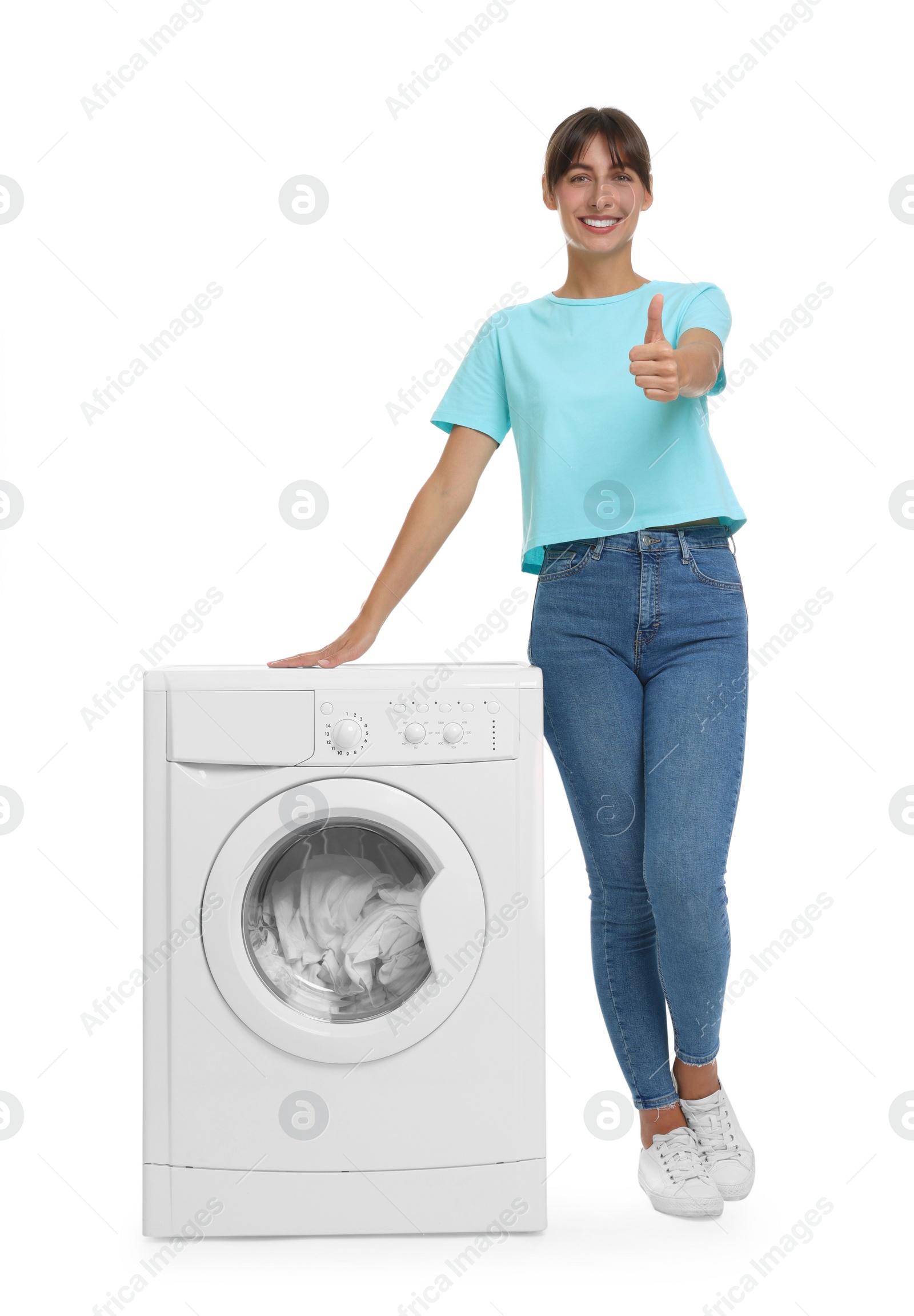 Photo of Beautiful woman showing thumbs up near washing machine with laundry on white background