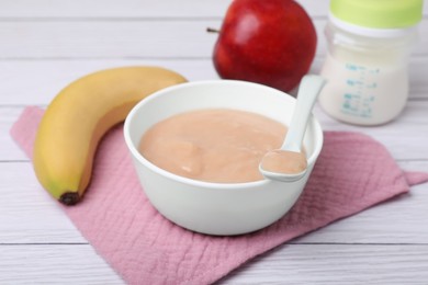 Bowl with healthy baby food and ingredients on white wooden table, closeup