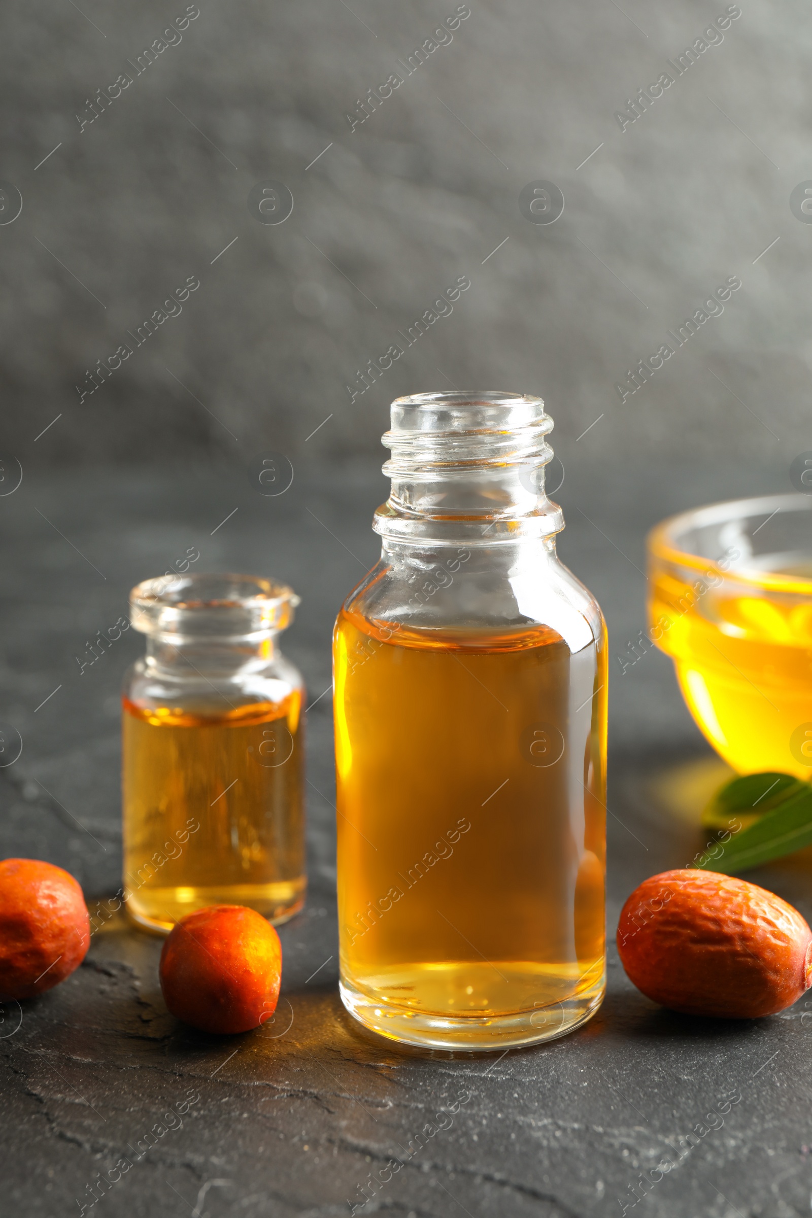 Photo of Jojoba oil and seeds on dark grey table