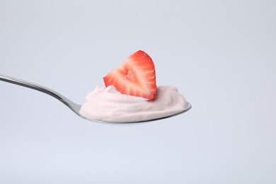 Photo of Delicious natural yogurt with fresh strawberry in spoon on light background