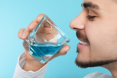 Man with glass of mouthwash on color background, closeup. Teeth and oral care