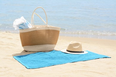 Photo of Bag with blanket, beach towel and straw hat on sandy seashore