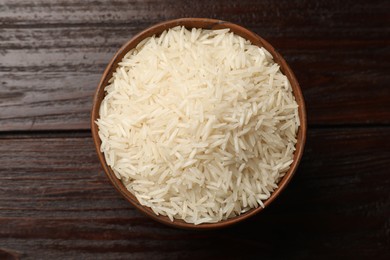 Photo of Raw basmati rice in bowl on wooden table, top view