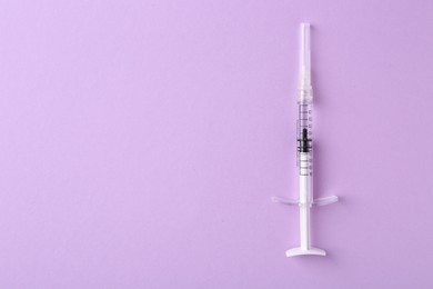 Photo of Cosmetology. One medical syringe on violet background, top view