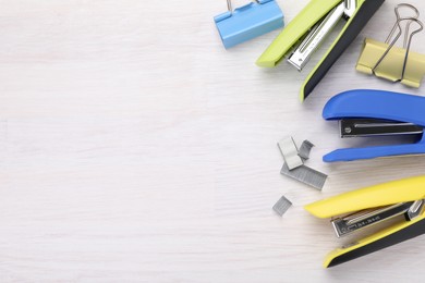 Photo of Bright staplers with staples and binder clips on light wooden table, flat lay. Space for text