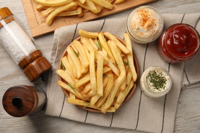 Delicious french fries served with sauces on light wooden table, flat lay