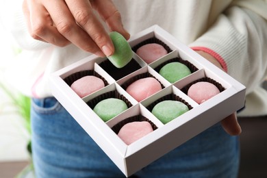 Woman holding delicious mochi above box, closeup