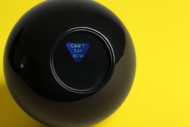 Photo of Magic eight ball with prediction Can't Say Now on yellow background, closeup. Space for text