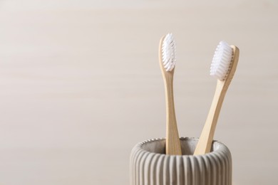 Photo of Bamboo toothbrushes in holder on light background, closeup. Space for text