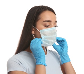 Woman in medical gloves putting on protective face mask against white background