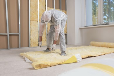 Photo of Worker measuring and cutting insulation material indoors