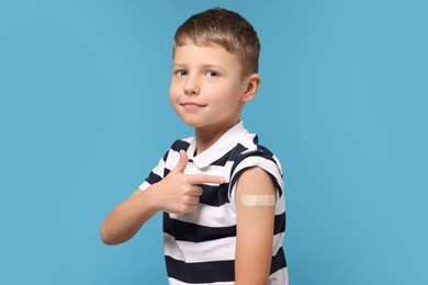 Boy pointing at sticking plaster after vaccination on his arm against light blue background