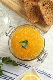 Photo of Fresh pike caviar in glass jar, bread and parsley on light wooden table, top view