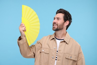 Photo of Happy man holding hand fan on light blue background